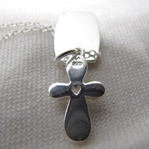 Puede incluir: Collar de plata con un colgante de cruz y un peque&ntilde;o coraz&oacute;n recortado. La cruz tiene una etiqueta con el n&uacute;mero "925" en ella.