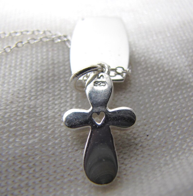 Puede incluir: Collar de plata con un colgante de cruz y un peque&ntilde;o coraz&oacute;n recortado. La cruz tiene una etiqueta con el n&uacute;mero "925" en ella.