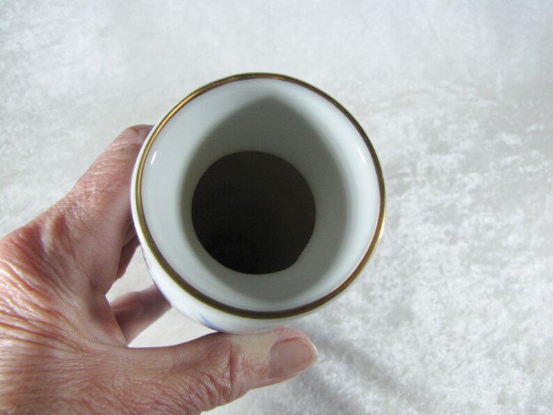 May include: White porcelain vase with a gold rim and blue floral pattern. The vase is empty and the inside is visible.