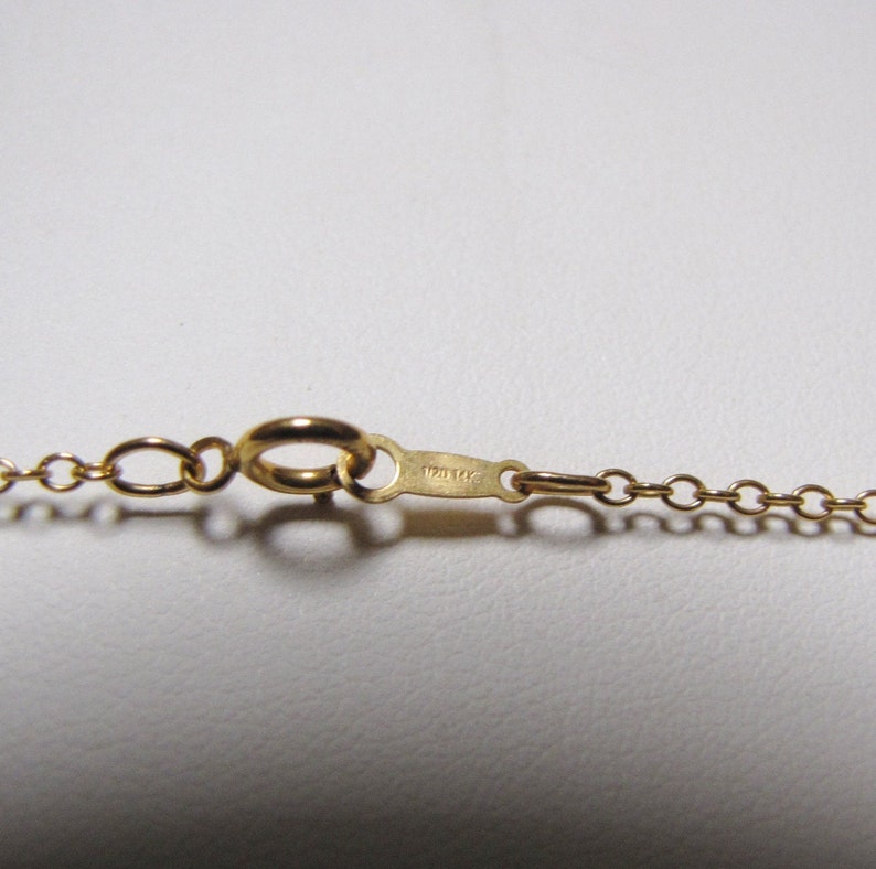 May include: A gold chain necklace with a lobster clasp closure. The clasp has the inscription "12K GF" on it.