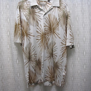 May include: A short-sleeved polo shirt with a white background and a repeating pattern of brown palm fronds. The shirt has a gray collar and a button-up neckline. The shirt is made of a lightweight material.