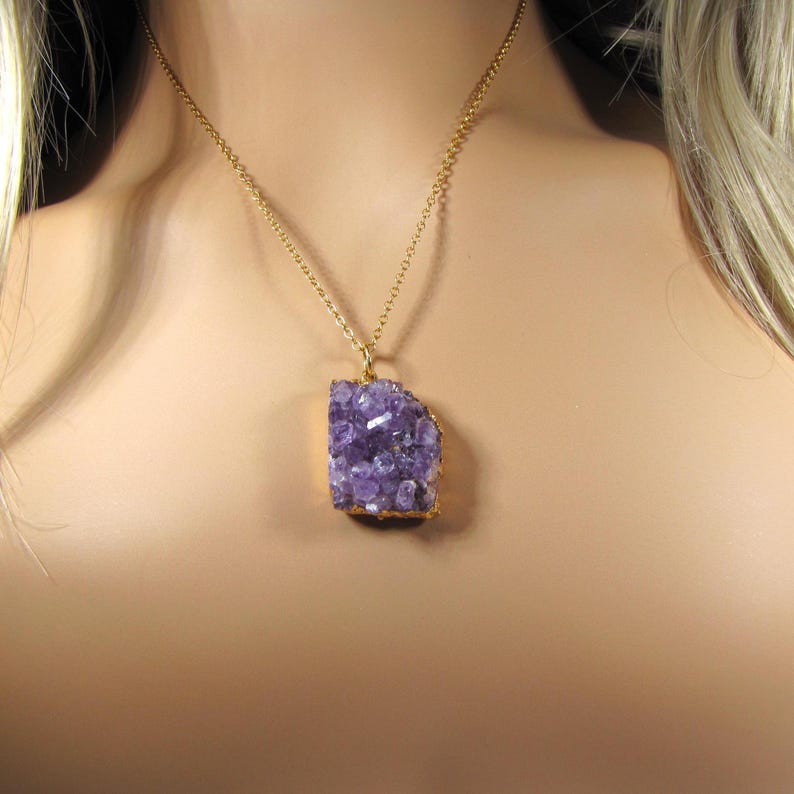 May include: A gold chain necklace with a large amethyst pendant. The amethyst is a natural crystal with a rough, irregular shape and a deep purple color.