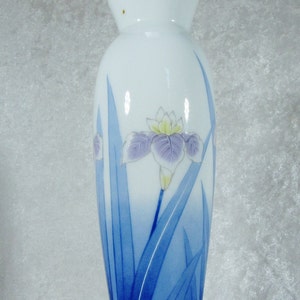 May include: A white ceramic vase with a blue and white floral design. The vase features a single iris flower with blue leaves.