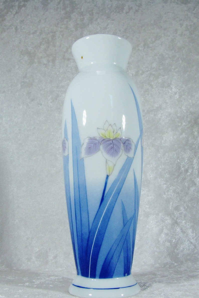 May include: A white ceramic vase with a blue and white floral design. The vase features a single iris flower with blue leaves.