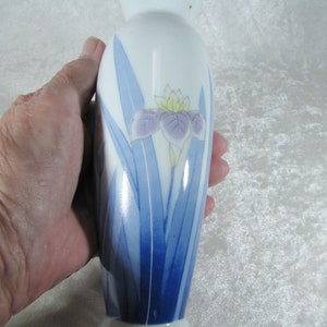 May include: A white porcelain vase with a blue and purple iris flower design. The vase is approximately 6 inches tall.