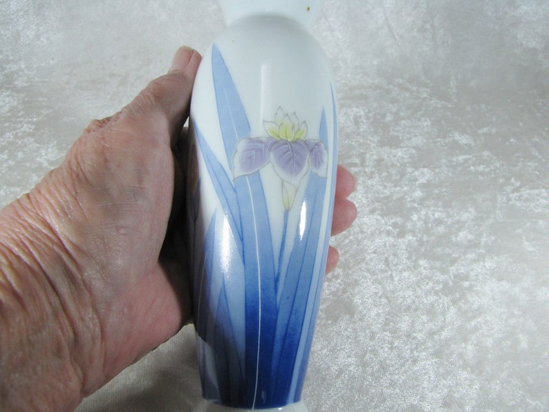 May include: A white porcelain vase with a blue and purple iris flower design. The vase is approximately 6 inches tall.