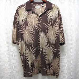 May include: Brown short-sleeved polo shirt with a palm leaf pattern in shades of tan and brown. The shirt has a collared neckline and a button-up placket. The shirt is made of a lightweight fabric.