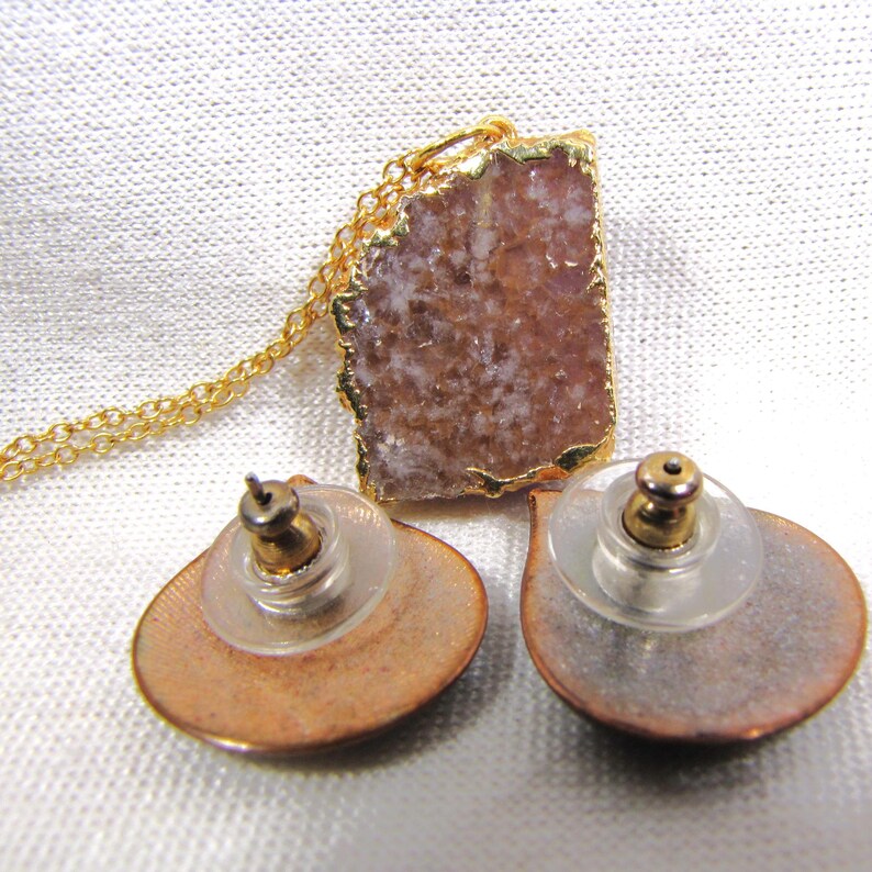 May include: A gold chain necklace with a pink and white agate pendant. The pendant is set in gold and has a rough, natural texture. The necklace comes with a pair of matching earrings with a similar design.
