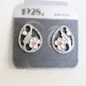 May include: A pair of silver tone earrings with a floral design. The earrings feature a pink flower with a rhinestone center, green leaves, and a white pearl. The earrings are packaged on a gray card with the text "1928" and "Made in USA".