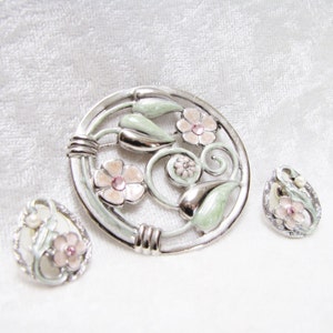 May include: A silver and green enamel brooch with pink flowers and rhinestones. Two matching earrings with the same design are also included.