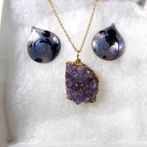 May include: A gold chain necklace with a large amethyst pendant and a pair of matching earrings with blue and silver enamel.