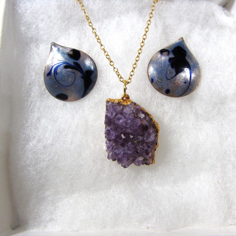 May include: A gold chain necklace with a large amethyst pendant and a pair of matching earrings with blue and silver enamel.