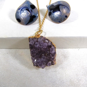 May include: A gold chain necklace with a large amethyst crystal pendant and a pair of matching earrings with blue and silver enamel.