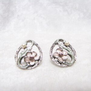 May include: A pair of silver earrings with a pink flower and a pearl accent. The earrings are in the shape of a circle with a floral design.