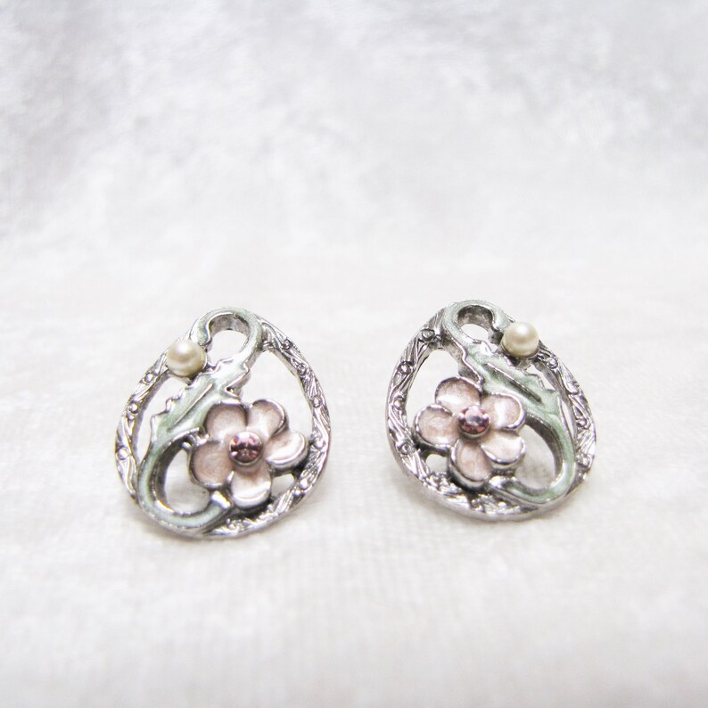 May include: A pair of silver earrings with a pink flower and a pearl accent. The earrings are in the shape of a circle with a floral design.