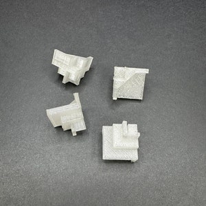 May include: Four white plastic 3D printed corner pieces for building a model or miniature. The pieces are in different shapes and sizes.