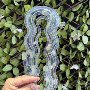 May include: A set of four clear, iridescent acrylic templates featuring a wavy, arched design. Each template has a distinct size, nested within one another, with a smooth, curved edge. The material reflects light with a subtle rainbow sheen.