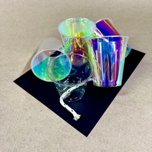 May include: A group of iridescent plastic cups, some with a textured design, on a black surface. The cups are stacked and overlapping, creating a colorful and abstract composition.