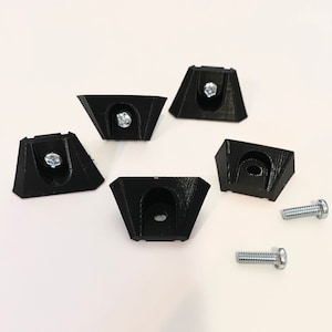 Puede incluir: Cinco soportes de esquina de plástico negro con un agujero para tornillo en el centro de cada uno. También se incluyen dos tornillos plateados.