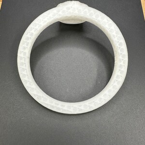 May include: White plastic ring with a textured surface. The ring is circular and has a raised center section.