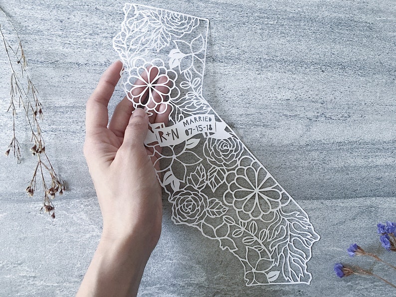 May include: White paper cut-out of the state of California with a floral design. A banner across the bottom reads "Married R+N 07-15-18".