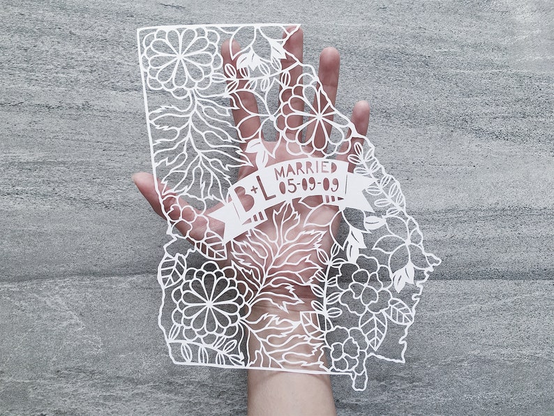 May include: White paper cut-out of the state of Georgia with floral designs and a banner that reads "B+L Married 05-09-09".