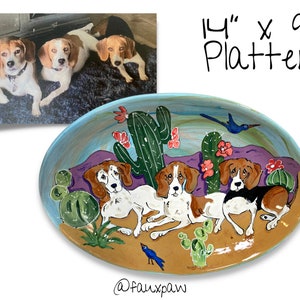 May include: A 14" x 9" oval ceramic platter with a hand-painted design of three beagle dogs in a desert landscape with cacti and a bluebird. The dogs are brown, white, and black with white markings. The platter has a light blue rim and a brown background.
