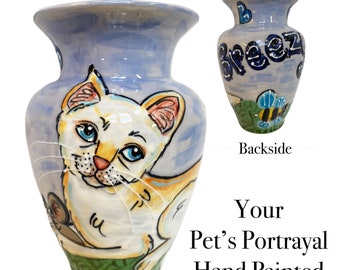 May include: Hand-painted ceramic vase with a light blue background and a white cat portrait. The vase has a lid and a design of a bee and the word "Breezy" on the back. The base is green.