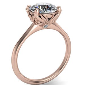 May include: A rose gold engagement ring with a large, round, clear diamond set in a floral design. The band is simple and smooth.