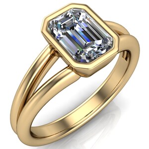May include: A gold ring with a large, emerald-cut diamond set in a bezel setting. The ring has a split shank.