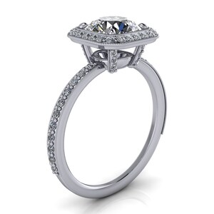 Puede incluir: Un anillo de compromiso de plata con un gran diamante redondo central rodeado por un halo de diamantes más pequeños. La banda también está engastada con diamantes más pequeños.