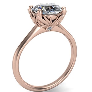 May include: A rose gold engagement ring with a large, round, clear diamond set in a floral design. The band is simple and smooth.