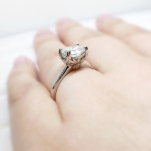 May include: A silver engagement ring with a large, round, clear gemstone set in a floral-inspired setting.