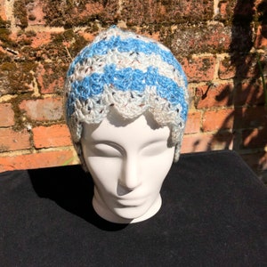 May include: A white and blue crocheted hat with a scalloped edge. The hat is on a white mannequin head.