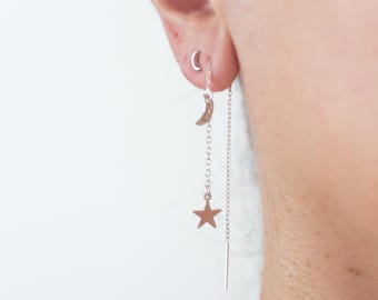 May include: A silver-toned threader earring featuring a delicate chain that suspends a small crescent moon charm and a five-pointed star charm. The earring is worn through the earlobe, with a straight metal post extending from the chain.