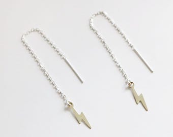 May include: A pair of silver-colored threader earrings, each featuring a delicate chain that suspends a small, flat lightning bolt charm at the end. The earrings have a polished metallic finish and a simple, slender design for ear piercings.