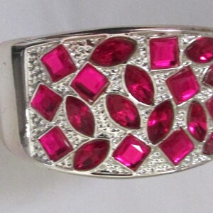 May include: A silver ring featuring a large pink stone set in the centre. The stone is surrounded by smaller pink stones.