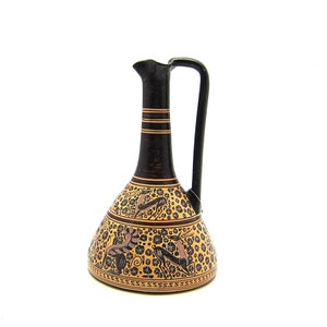 May include: A black and brown ceramic pitcher with a geometric design and floral patterns. The pitcher has a wide base and a narrow neck with a handle.