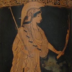 Puede incluir: Un jarr&oacute;n griego negro y naranja con una representaci&oacute;n de una mujer con casco y sosteniendo una lanza y una antorcha. La mujer lleva una t&uacute;nica a rayas y una capa.
