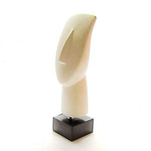 Op de afbeelding: Witte keramische sculptuur van een gestileerd mensenhoofd met een lange neus, op een zwarte vierkante basis.