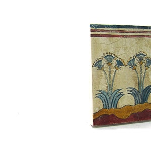 May include: A close-up of a decorative tile with a painted design of blue and yellow flowers on a beige background. The tile has a red and white border.