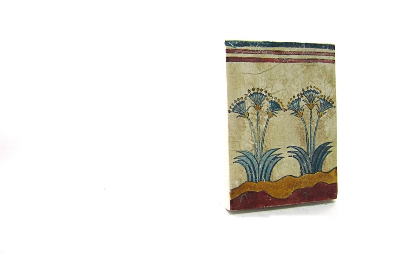 May include: A close-up of a decorative tile with a painted design of blue and yellow flowers on a beige background. The tile has a red and white border.