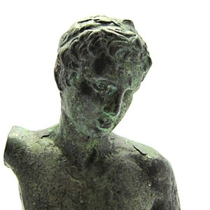 Pu&ograve; includere: Una scultura in bronzo di un torso maschile, con la testa inclinata verso il basso. La scultura &egrave; usurata e ha una patina verde.