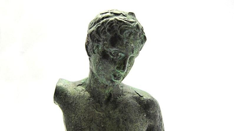 Pu&ograve; includere: Una scultura in bronzo di un torso maschile, con la testa inclinata verso il basso. La scultura &egrave; usurata e ha una patina verde.