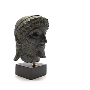 May include: Bronze sculpture of a man's head with a wreath on his head. The sculpture is on a black base.