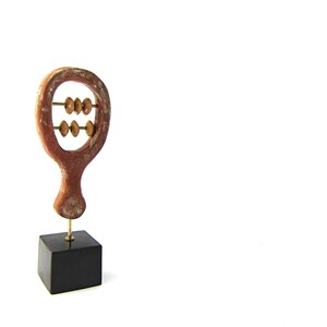 May include: A wooden abacus sculpture with a reddish-brown frame and brass beads. The abacus is mounted on a small black square base. The sculpture is a decorative item.