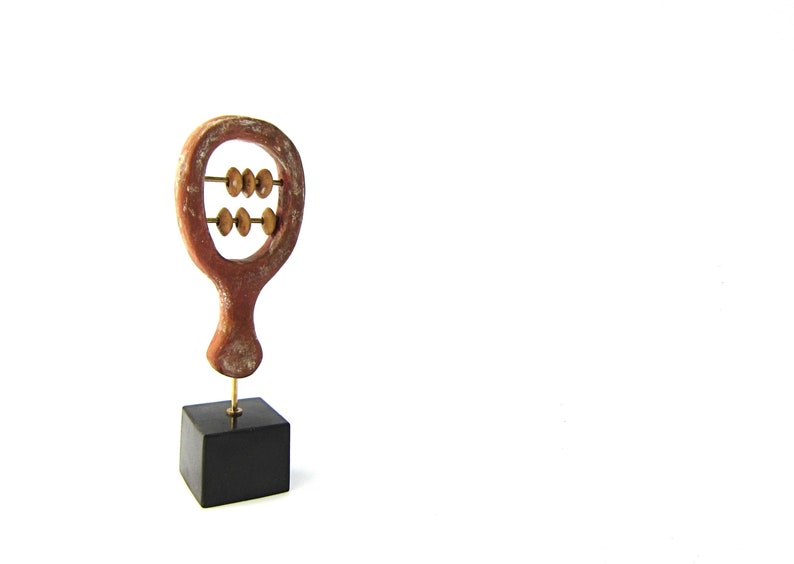 May include: A wooden abacus sculpture with a reddish-brown frame and brass beads. The abacus is mounted on a small black square base. The sculpture is a decorative item.