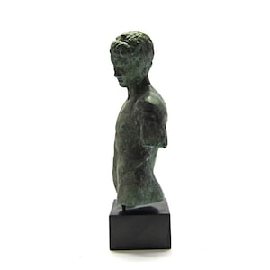 Pu&ograve; includere: Un busto di bronzo di un giovane uomo con una corona di alloro sulla testa. Il busto &egrave; su una base nera.