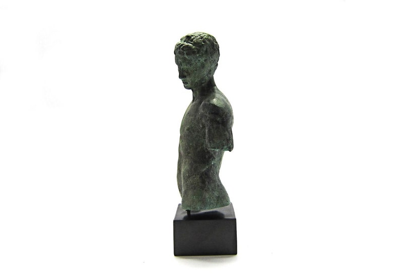 Pu&ograve; includere: Un busto di bronzo di un giovane uomo con una corona di alloro sulla testa. Il busto &egrave; su una base nera.