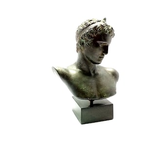 May include: Bronze bust sculpture of a young man with a laurel wreath on his head. The bust is on a black marble base.